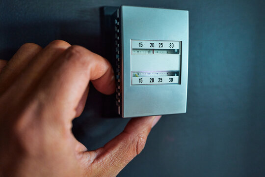 Hand Adjusting an Analog Thermostat on a Dark Blue Wall
