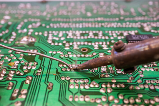 Soldering Iron Tip Touching Green PCB Circuit Board Closeup