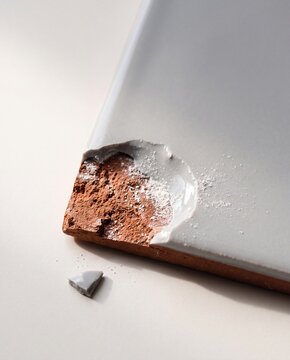 Broken Ceramic Tile Corner Showing Red Clay Base and White Glaze.
