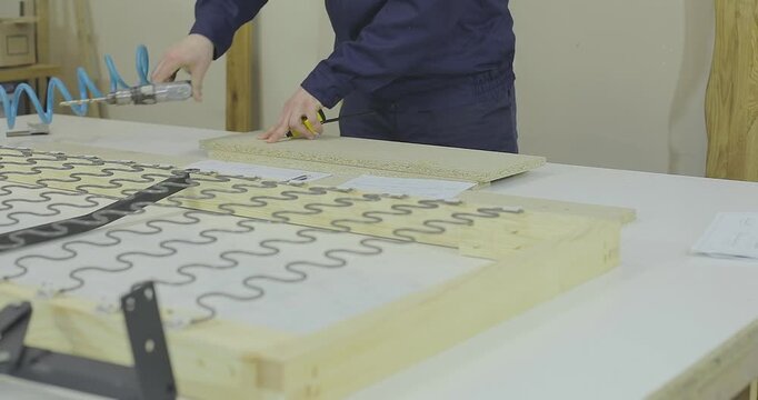 A furniture maker or furniture designer in blue workwear marking and preparing particle board parts on a workbench. Design and assembly of wooden and upholstered furniture.