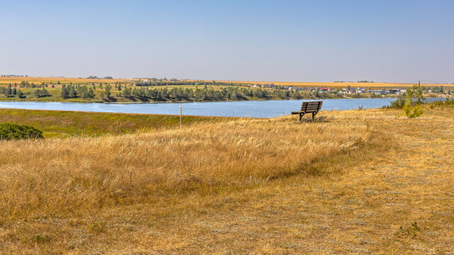 Peaceful Prairie Lake Landscape with Bench and Golden Summer Grass at Craik Regional Park in Saskatchewan, Canada