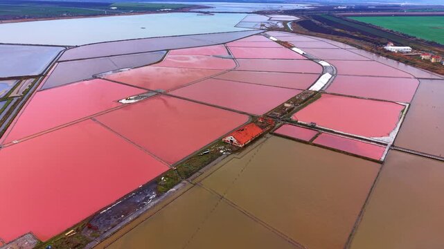 Salt pans with varying colors in a flat landscape during daylight hours. Salt pans display shades of pink and brown in a flat area under bright sunlight.