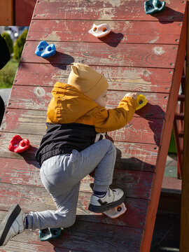 A 3-year-old boy is climbing up a wall, pretending to be a rock climber.