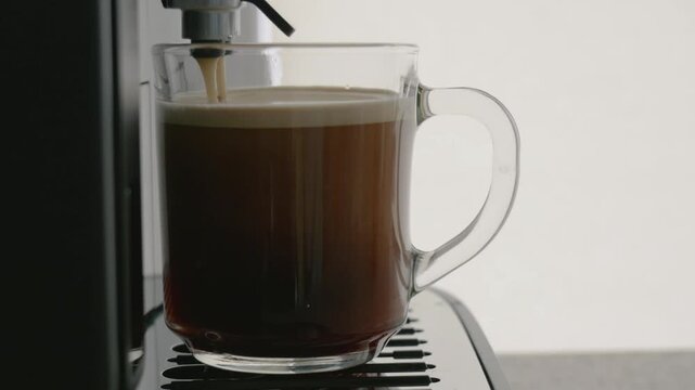 Coffee machine pouring fresh espresso into a glass mug