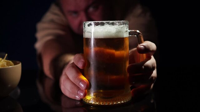 А man reaches for a mug of beer. Glass mug of light beer on a table with a blurred man reaching for the drink in a pub