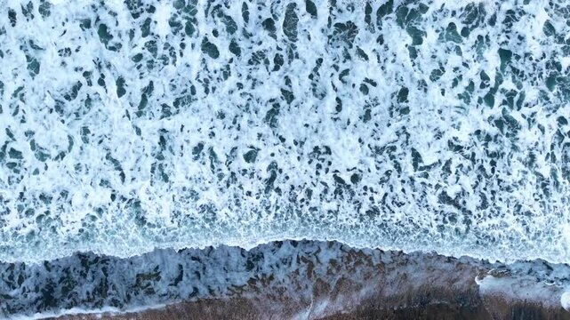Waves crash on the shore in a coastal area during daylight. The sea water creates waves that hit the sandy beach in daylight.