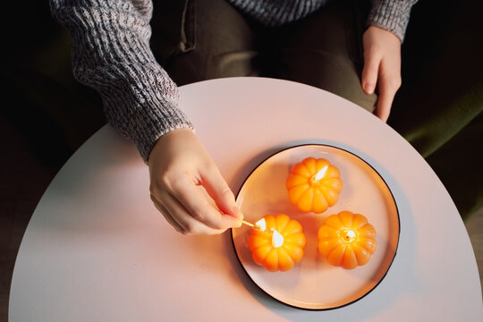 Top view of woman lighting pumpkin candles on plate for cozy home autumn decor