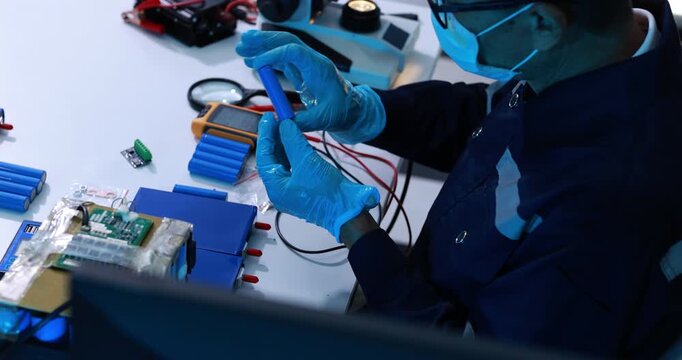 Technician wearing gloves and safety glasses tests an electronic circuit board with probes at a workbench in a modern repair laboratory.