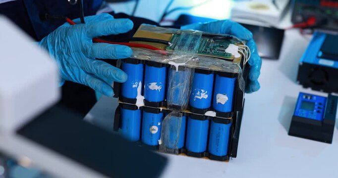 Gloved technician repairs a lithium battery pack with blue cylindrical cells and circuit board on a laboratory workbench.