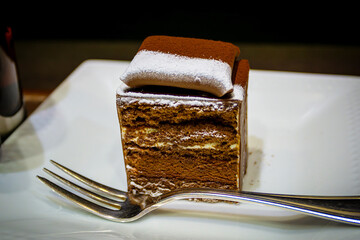 Popular Japanese fusion chocolate mousse and sponge black forest cake dessert sprinkled with icing sugar and served on a white plate with a fork in Osaka, Japan. © ronniechua