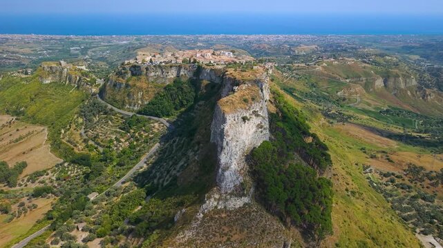 Gerace Calabria Italy 4k drone view of dramatic narrow rock ridge. Flyover along steep cliff spine revealing historic borgo village on hilltop, one of most beautiful villages in Italy