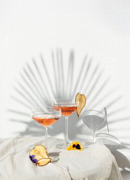 Two rose wine glasses with summer cocktails and dried fruit appetizers. Tropical light background with palm shadow.