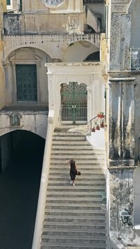 Woman walks historic stairs past Saint Salvador Church in Atrani, Amalfi Coast