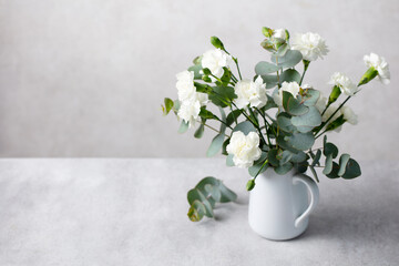 White carnation bouquet with eucalyptus leaves in a ceramic jug on grey concrete background. Copy space. © annapustynnikova