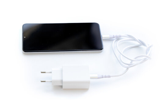 Modern smartphone connected to white power charger on surface