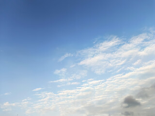 Wispy white clouds drift across a vast blue sky during a bright sunny day © Md
