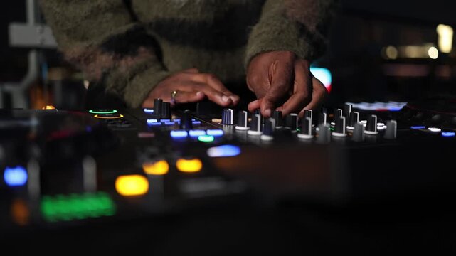 Professional DJ hands move across knobs faders and control elements on a music controller creating a dynamic live performance atmosphere on stage