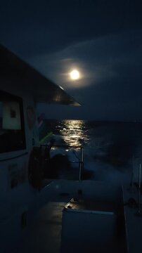   Un catamar&aacute;n navegando en el mar, con la luna llena brillando en el cielo y reflejando su luz sobre las olas del agua. Costa Blanca. Espa&ntilde;a. 
