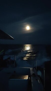  Un catamar&aacute;n navegando en el mar, con la luna llena brillando en el cielo y reflejando su luz sobre las olas del agua. Costa Blanca. Espa&ntilde;a. 