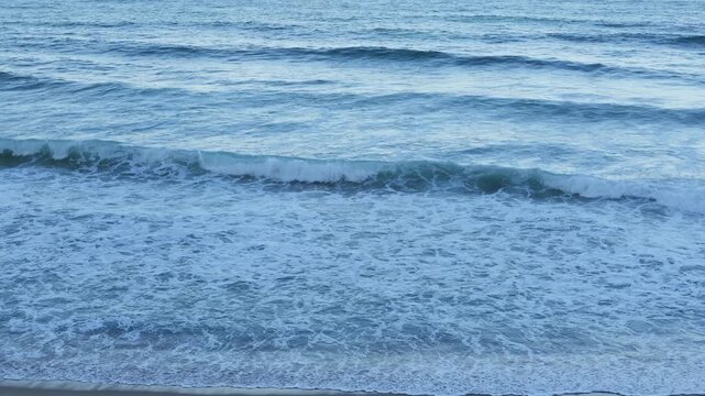 Close up background view of clear ocean water surf with white foam waves rolling over sandy beach shore in turquoise sea during sunny summer vacation travel