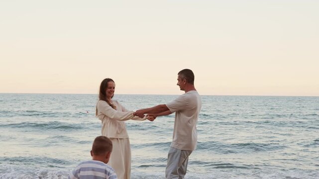 Loving couple holding hands and dancing on sandy sea beach shore during romantic evening walk at sunset