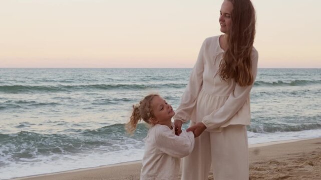 Happy mother and cute little daughter holding hands while walking together along sandy sea beach shore