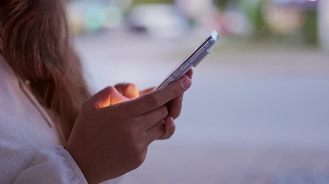 Close up of female hands holding smartphone and typing message on touch screen outdoors