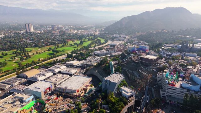 Drone panoramic footage moving from left to right, showing Universal Studios Hollywood theme park and film production area with surrounding golf course and mountains in Los Angeles, California. The