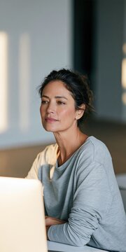 Thoughtful woman working at laptop in bright indoor home office portrait for business background and remote work banner