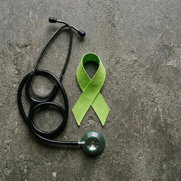 Green awareness ribbon and stethoscope on textured concrete background symbolizing mental health medical care and support