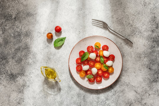 Caprese salad with mozzarella, colored cherry tomatoes and basil leaves on white rustic background, top view, flat lay, copy space