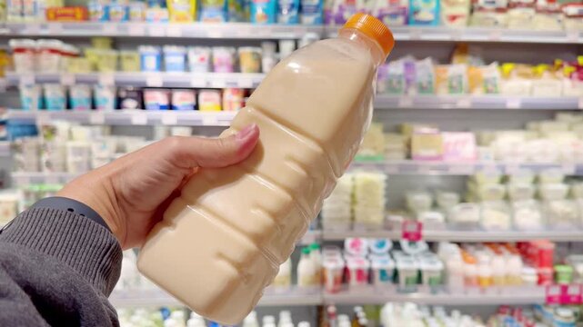 Hand Holding Milk Bottle in Supermarket &ndash; Dairy Products in Front of Blurred Shelves