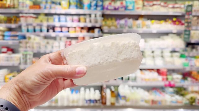 Hand Holding Cottage Cheese in Supermarket &ndash; Dairy Products in Front of Blurred Shelves
