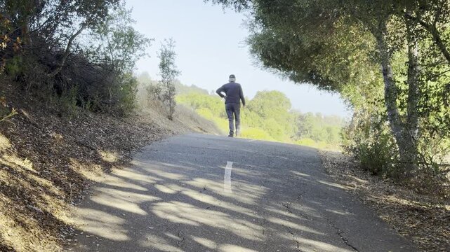 Senior man with hand on hip walks down a sloping path