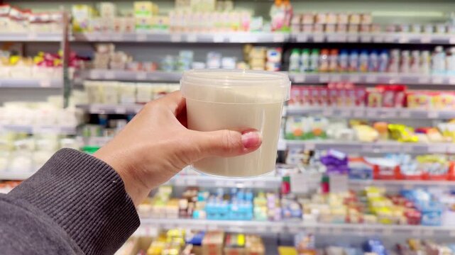 Hand Holding Cottage Cheese in Supermarket &ndash; Dairy Products in Front of Blurred Shelves