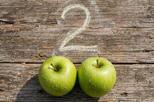Educational Concept of Number Two Written in Chalk with Two Green Apples on Wooden Background
