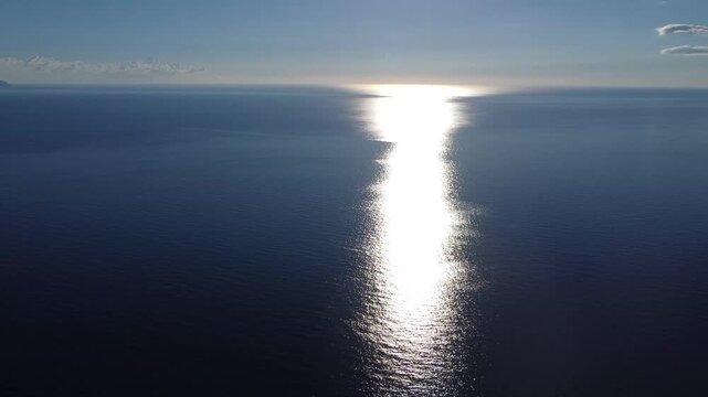 Aerial view of sunlight shimmering across the open ocean. Drone view of bright sun reflection on blue ocean water. Sunlight sparkling across the calm sea surface.