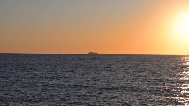 Passenger ship sailing across the open ocean during a stunning orange sunset. Large container vessel navigating calm waters against a dramatic evening sky.