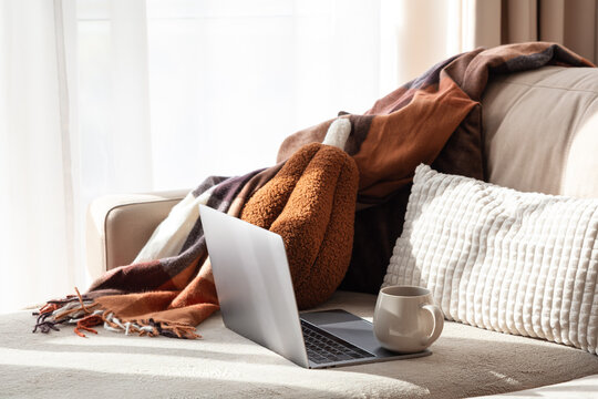 Cozy home office setup with laptop and warm blanket on sofa with natural light