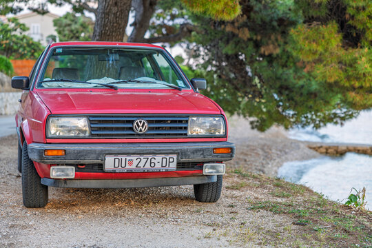 Red Volkswagen Jetta mk2 Parked On A Seaside Gravel Path Under Pine Trees