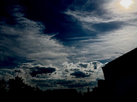 Features high-altitude, wispy Cirrus clouds stretching near the sun, layered above low-level, shadowed Cumulus and Stratocumulus clouds along the horizon