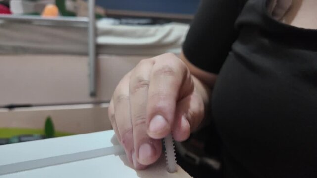 Person uses tool to attach small white object to furniture. Hands are steady, focused on precise task. Scene suggests home improvement or child room setup. Good for DIY, parenting