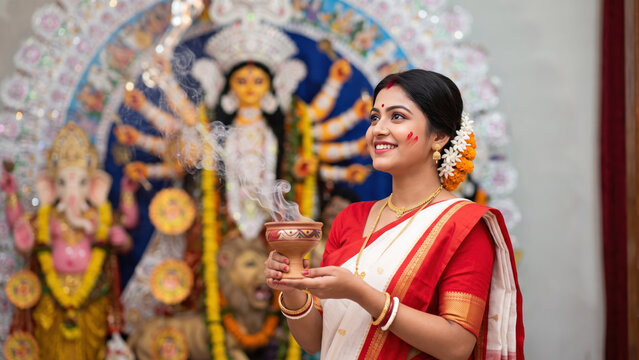 Woman holding a smoking dhunuchi at durga puja, white saree with a red border before a goddess idol, bengali incense offering ritual