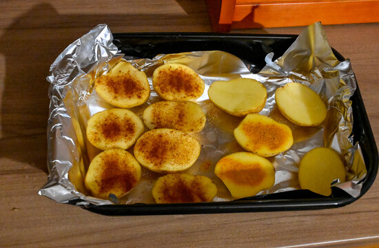 Peeled and sliced potatoes neatly prepared on a tray for oven baking. Raw potato pieces freshly cut and ready to be roasted in the kitchen.