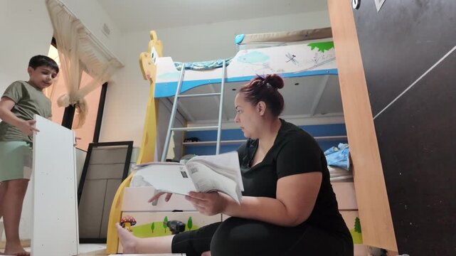 Mother and child in room, focused on assembly task. Child watches closely, shows curiosity and engagement. Mother guides with care, demonstrates patience and support. Perfect for home improvement