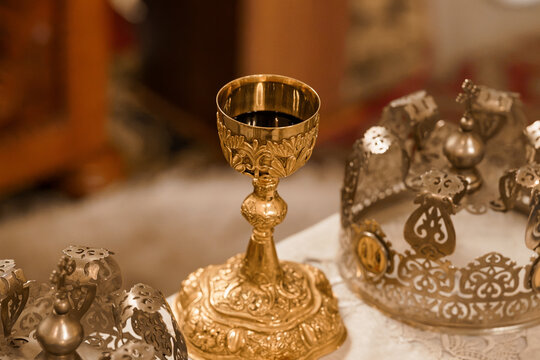 Ornate golden chalice with wine and silver crown ornaments on white altar cloth in church setting