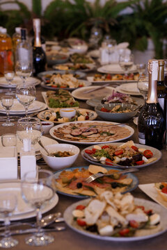 Elegant buffet table with diverse gourmet salads cold cuts wine glasses and champagne bottles set against blurred green foliage background