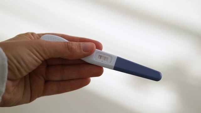 Close-up of hand holding home pregnancy test with two visible lines as positive result. Pregnancy health care, fertility, family planning and conception. Ovulation, fetus, motherhood, childbirth.