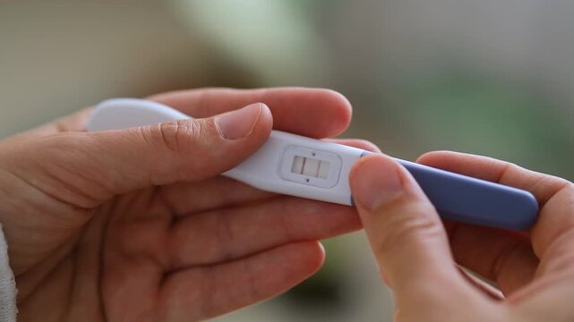 Close-up of hands holding home pregnancy test with two visible lines as positive result. Pregnancy health care, fertility, family planning and conception. Ovulation, fetus, motherhood, childbirth.