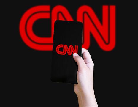 Hand holding smartphone with CNN logo on screen against blurred backdrop, illustrative editorial